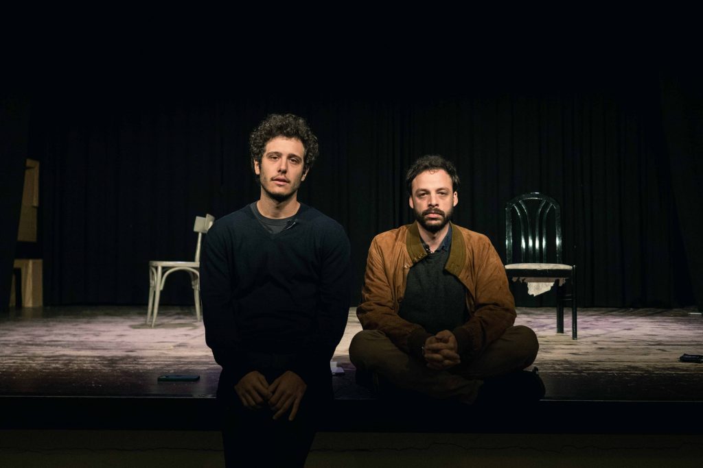 Due uomini, Nicola Borghesi e Enrico Baraldi, sono seduti sul bordo di un palcoscenico e fissano la fotocamera.