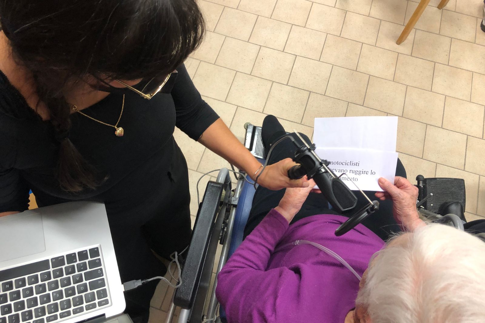 Una signora con computer e microfono in mano intervista un'anziana della casa della di riposo.