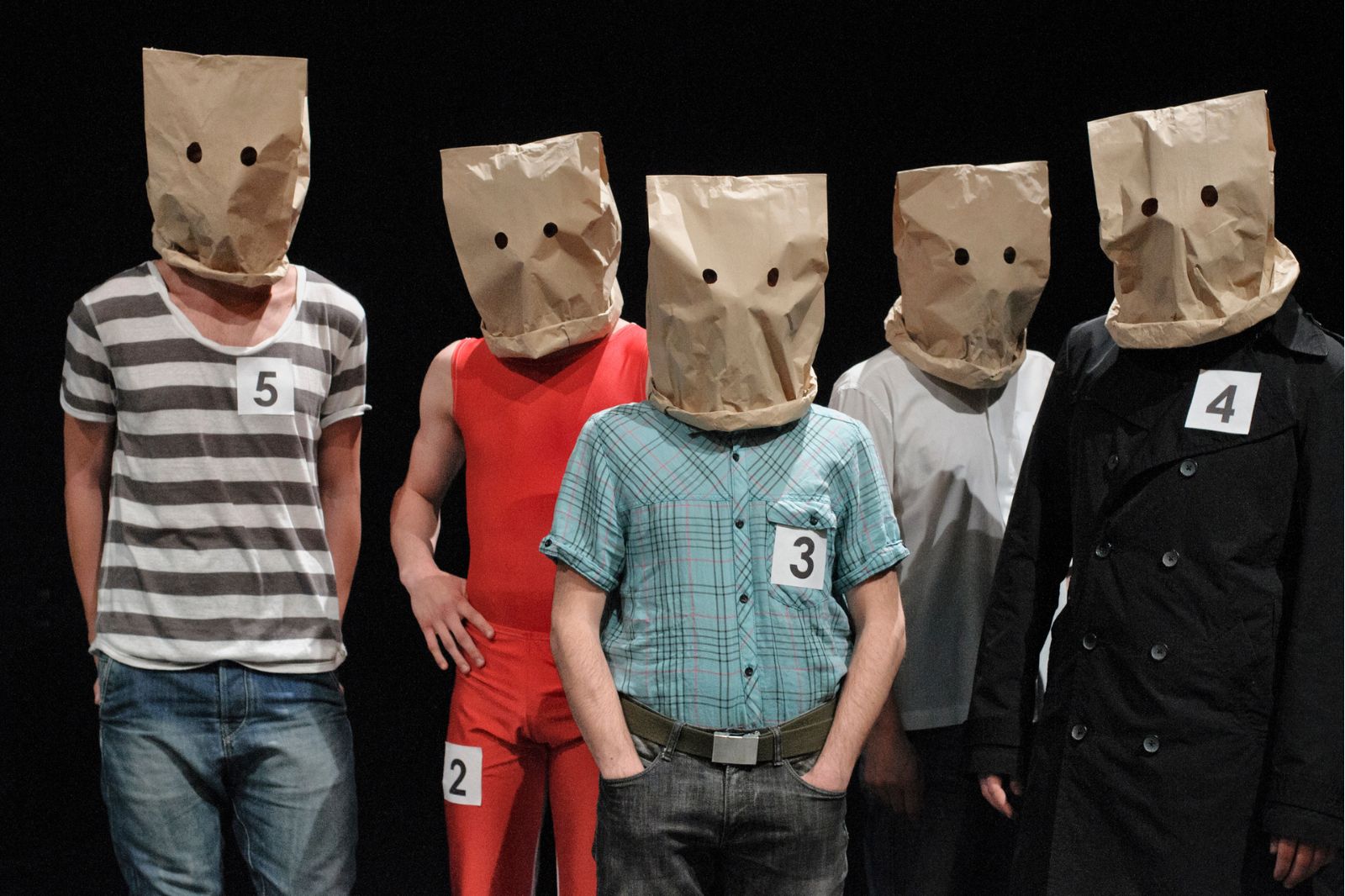 In foto, cinque uomini in riga portano sulla testa sacchetti di carta con buchi per gli occhi