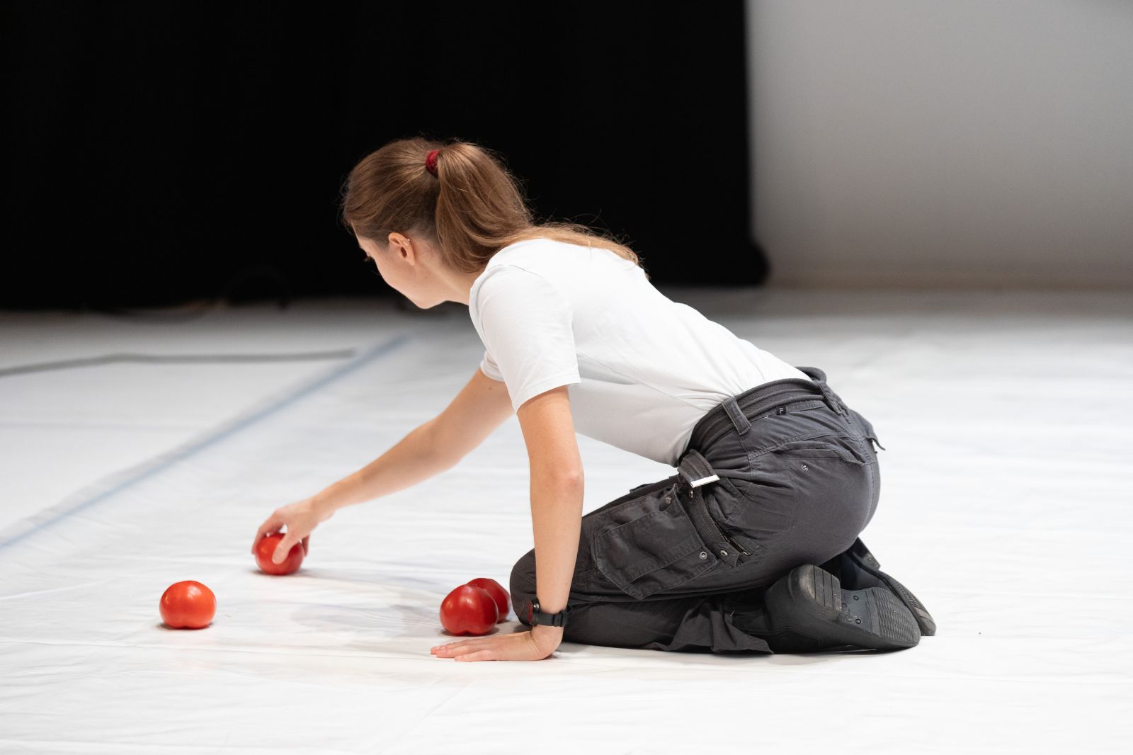 In foto, una ragazza posiziona tre pomodori su un tappeto danza bianco
