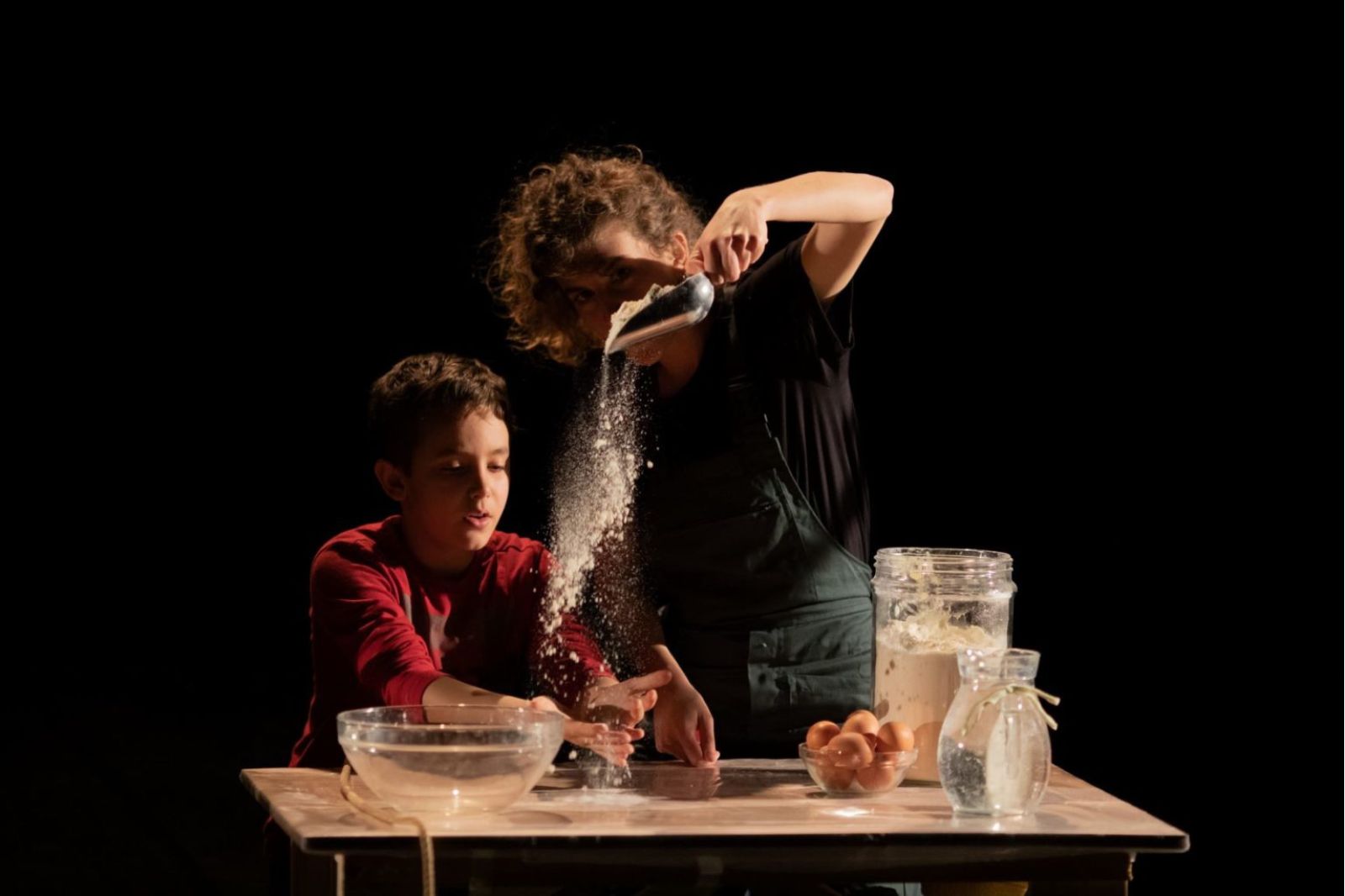 In foto, una donna e un bambino intenti a cucinare. Sul tavolo farina, uova, acqua
