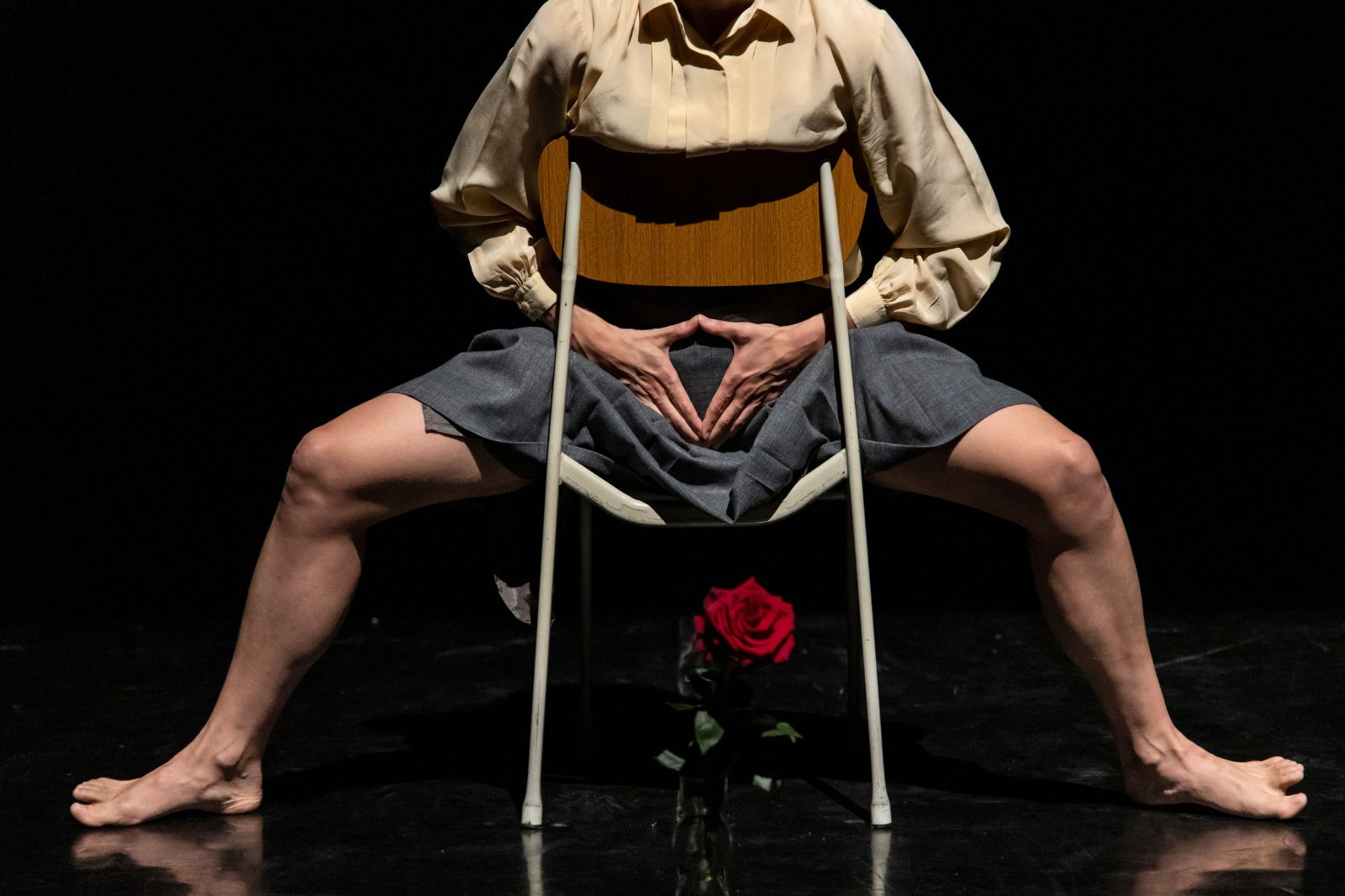 In foto, una donna seduta a gambe aperte su una sedia al contrario. Davanti a lei una rosa rossa